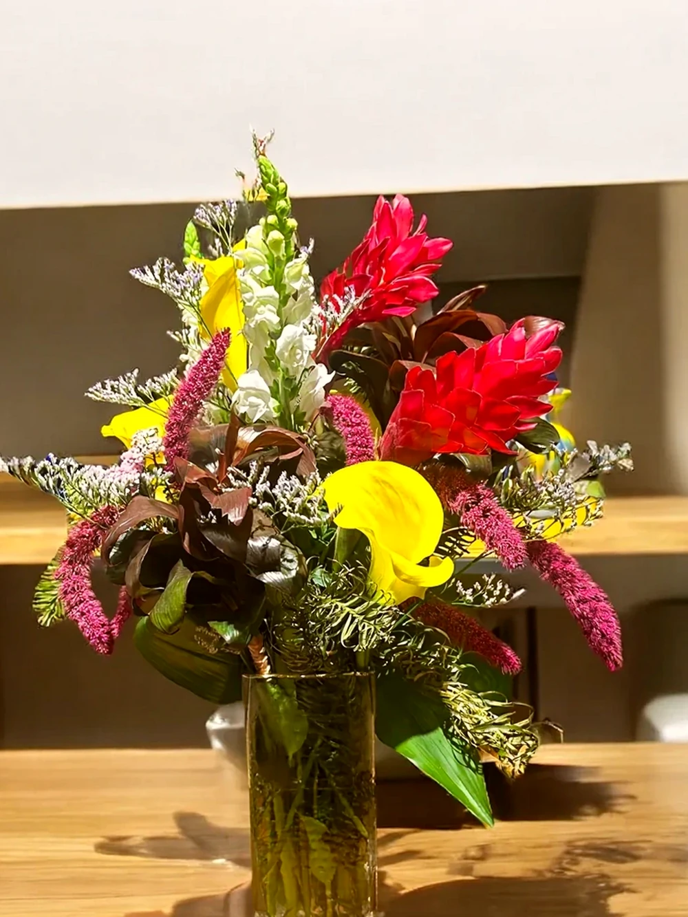 Arranjo Floral Tropical com Callas Amarelas e Alpínias no Vaso de Vidro Retangular, imagem ilustrativa