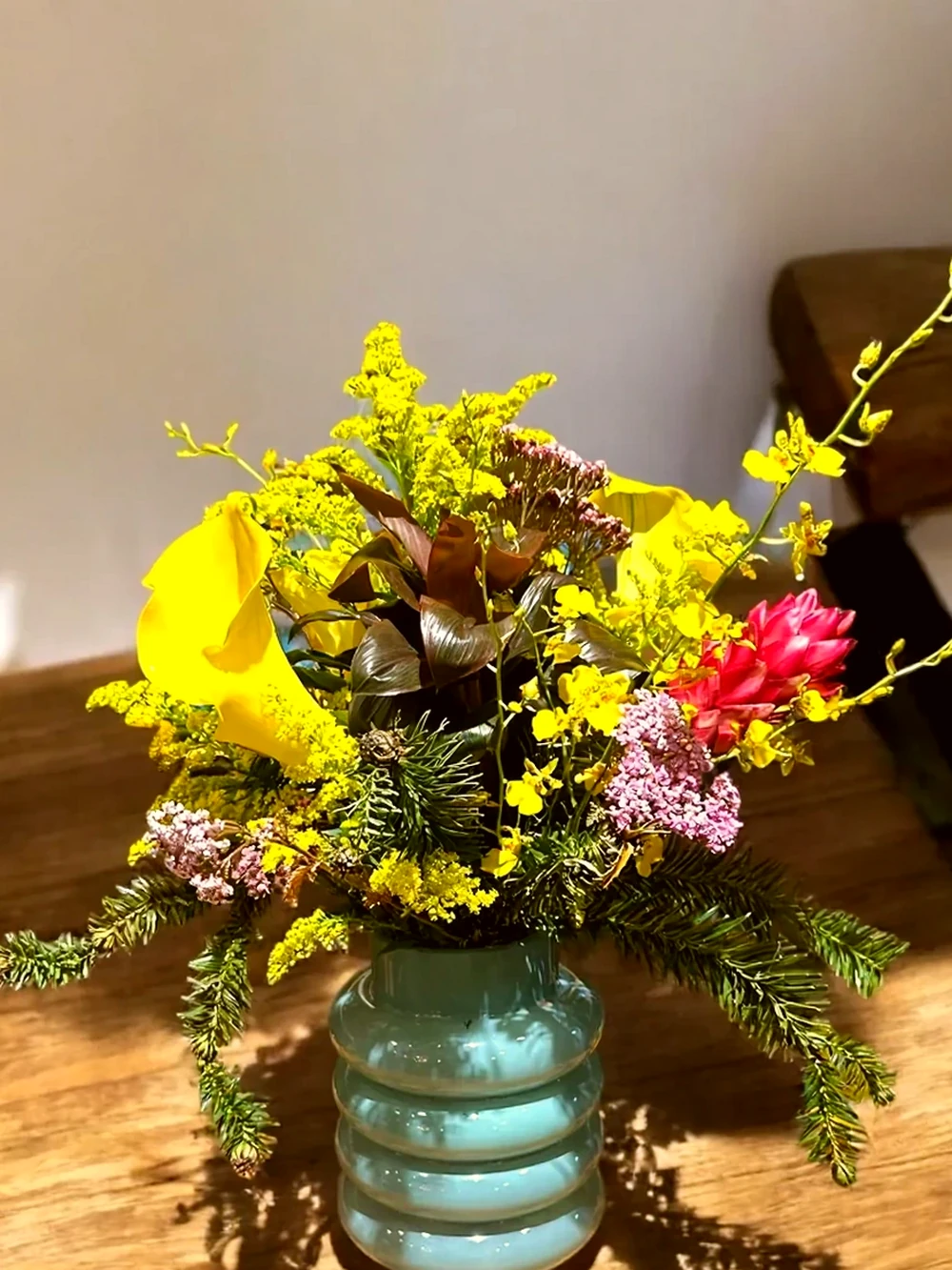 Arranjo Floral com Callas Amarelas e Flores Tropicais no Vaso de Vidro Azul, imagem ilustrativa